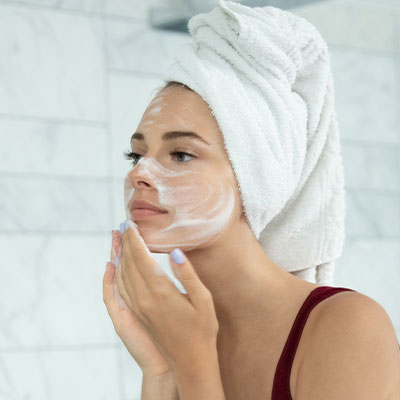 A woman cleansing her face with a towel on her head.