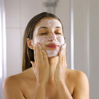 A woman applying a Pevonia cleanser to her face.