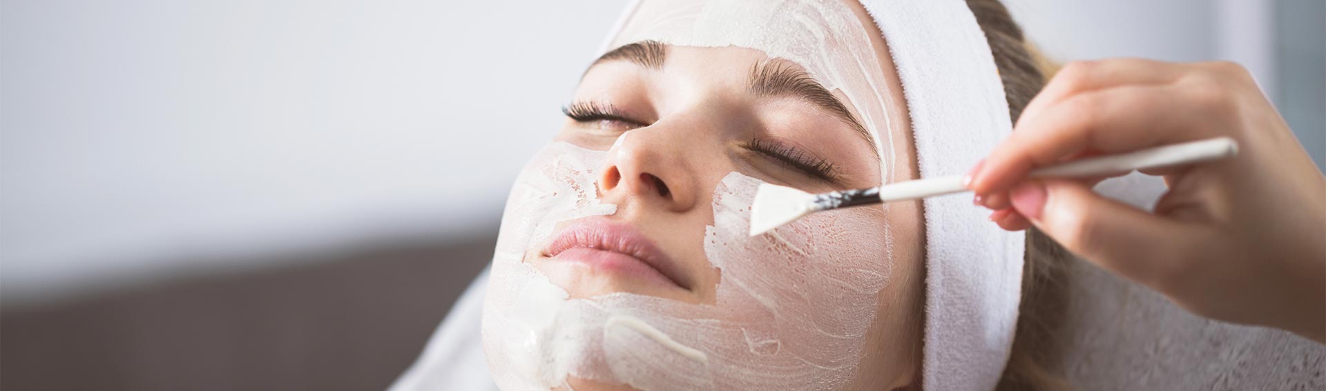 Woman receiving a facial treatment, being applied with a brush, at a spa.